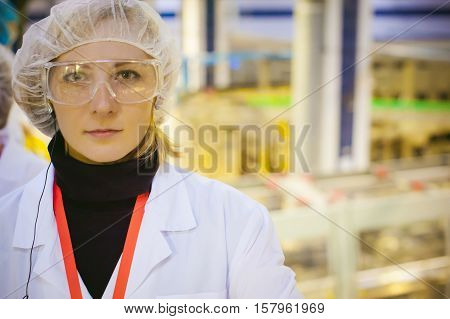 Female Worker On The Production Line Of Beer Factory. Portrait Of A Woman In A White Robe, Standing