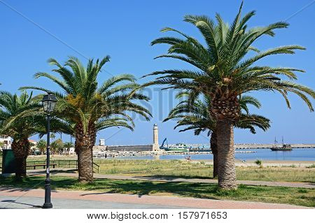 RETHYMNO, CRETE - SEPTEMBER 15, 2016 - View of the lighthouse framed by palm trees with tourists along the harbour wall Rethymno Crete Greece Europe, September 15, 2016.