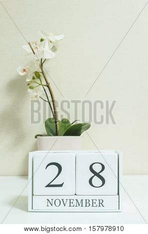 Closeup white wooden calendar with black 28 november word with white orchid flower on white wood desk and cream color wallpaper in room textured background selective focus at the calendar