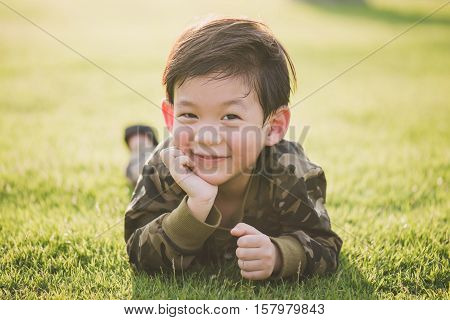Cute Asian child lying on greeen grass under sun light