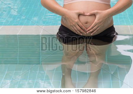 Pregnant woman hands holding belly on swimming pool background healthy concept.