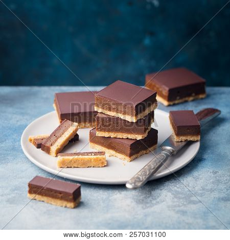 Chocolate Caramel Slices, Bars, Millionaires Shortbread On A Plate. Blue Background. Copy Space