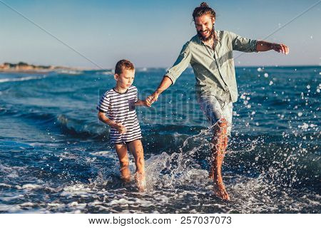 Happy Father And Son, Man & Boy Child, Running And Having Fun In The Sand And Waves Of A Sunny Beach