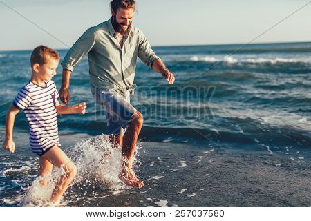 Happy Father And Son, Man & Boy Child, Running And Having Fun In The Sand And Waves Of A Sunny Beach