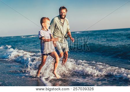 Happy Father And Son, Man & Boy Child, Running And Having Fun In The Sand And Waves Of A Sunny Beach