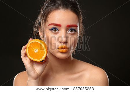 Young woman with dyed eyebrows and half of orange on black background