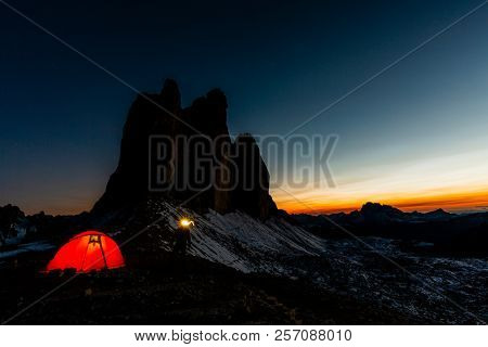 Night bivouac at Tre Cime di Lavaredo, milion star hotel under night sky, red iluminated tent on pass in Dolomites, Italy.