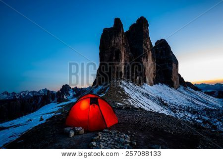 Night bivouac in early winter at Tre Cime di Lavaredo, milion star hotel under night sky, red illuminated tent on pass in Dolomites, Italy.