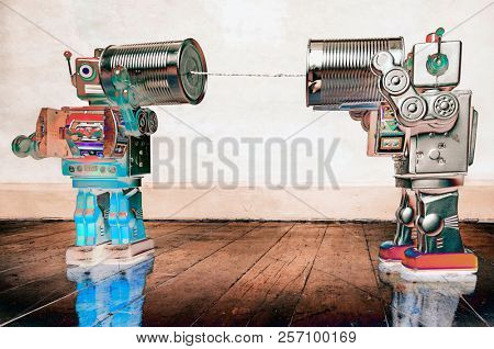 Two retro  Robots toys talking on tin can phones on an old wooden floor 