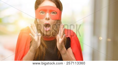 Middle age super hero woman wearing red mask and cape stressful keeping hands on head, terrified in panic, shouting