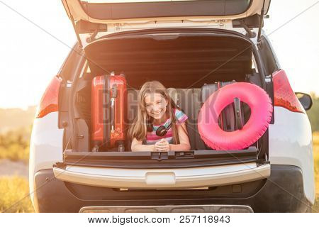 Girl smiling and lying in the car trunck with lifebuoy and suitcase