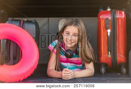 Girl smiling and lying in the car trunck with lifebuoy and suitcase