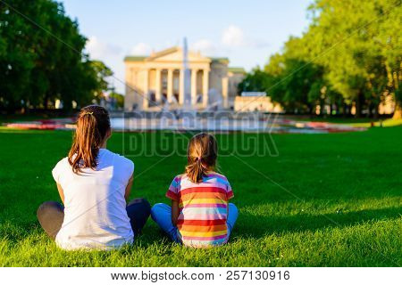 Children Sitting On The Grass In The Park In Front Of Neoclassical Opera House Located In Poznan, Po