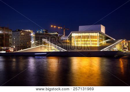 OSLO, NORWAY - JULY 24, 2018: Oslo Opera House (Operahuset),  home of The Norwegian National Opera and Ballet and the national opera theatre with Barcode buildings in background at night