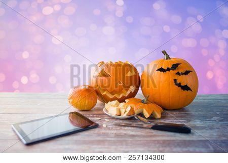 holidays, halloween and technology concept - jack-o-lantern or carved pumpkin with tablet pc computer and knife on wooden table over lights background