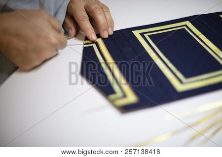 Book Binder Hand Working A Pattern On The Blue Cover Of A Hardcover Book In His Workshop In A Close 
