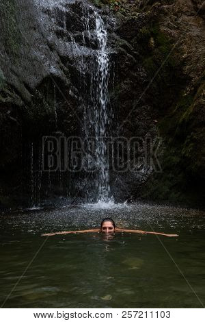 Young Beautiful Teenage Girl Swimming And Enjoying The Cold Waterfall Water. Millomery Waterfalls Cy