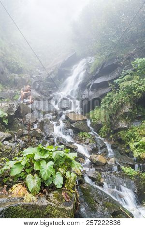 Portrait Of A Man Sitting By The Waterfall With A Smartphone In His Hand