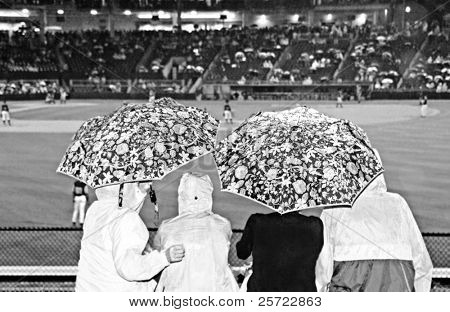 Rodina sleduje baseball hra pod deštníkem během deště