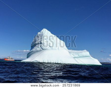 Tour Boat Viewing Massive Iceberg Off The Coast Of Twinlingate, Newfoundland And Labrador, Canada