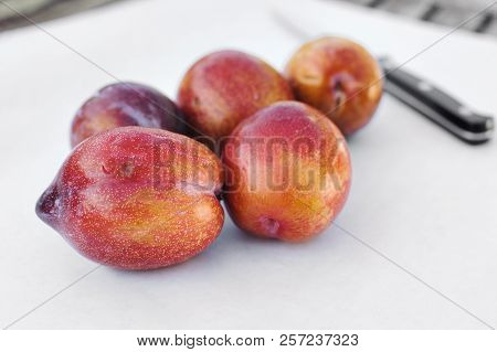 Five Amigo Pluot Fruits On White Paper With A Knife