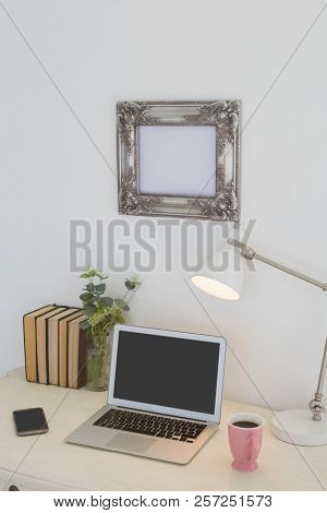 Electronic gadgets, lamp, book, mug, flora and book on table against white wall