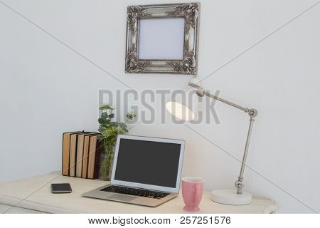 Electronic gadgets, lamp, book, mug, flora and book on table against white wall