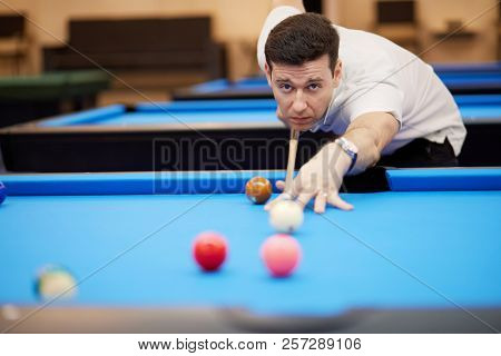 Man aims white ball with cue stick on pool table in club.