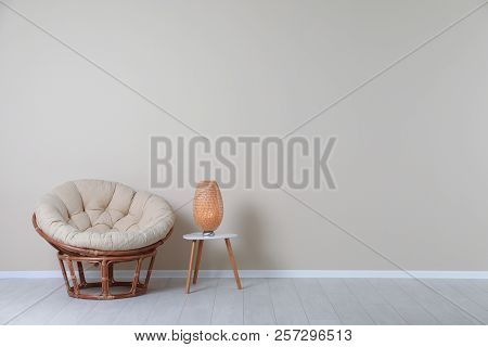 Comfortable Papasan Chair And Lamp On Table Near Color Wall With Space For Text. Interior Element