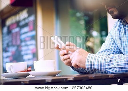 Man Using A Cell Phone On Cafe Terrace And Drinking Coffee. Man Drinks Coffee. Man Using Cellphone. 
