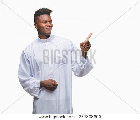 Young arabic african man wearing traditional djellaba over isolated background with a big smile on face, pointing with hand and finger to the side looking at the camera.