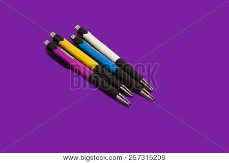 Four Different New Bright Colored Pens Lying On A Purple Background. Concept Of Office Supplies. Fre