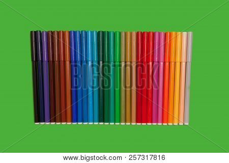 Line Of Various Bright Plastic Multicolored Felt Pens Lying On A Green Surface. Concept Of Creativit