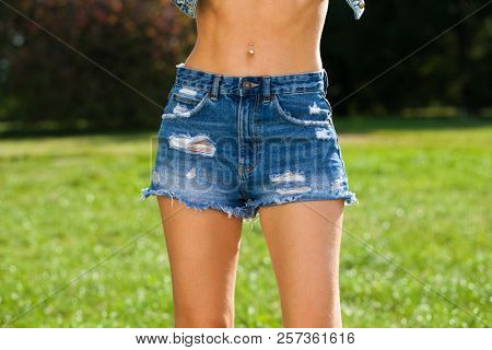 Part of the body, front view torn blue jeans shorts for women on the background summer park