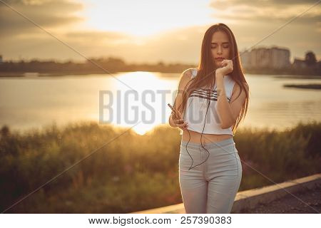 Young Beautiful Caucasian Girl Listening To Music With Smartphone Walking In The City With Headphone