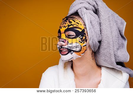 A Funny Young Girl With A Towel On Her Head Wants To Be Beautiful, On Her Face A Moisturizing Mask W