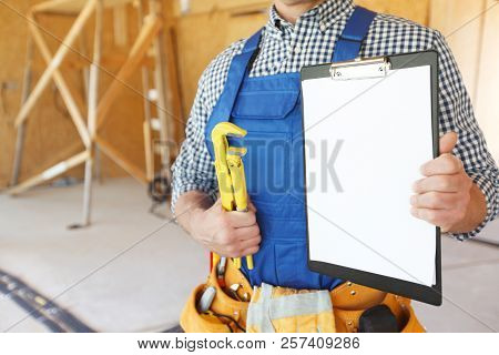 Worker With A Monkey Wrench And Clipboard At Construcion Site