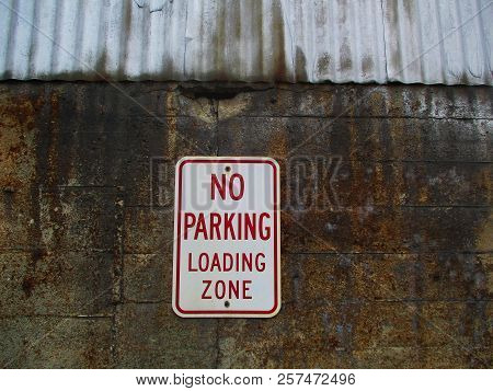 A Red And White No Parking Sign On A Concrete Wall Under A Sheet Metal Roof