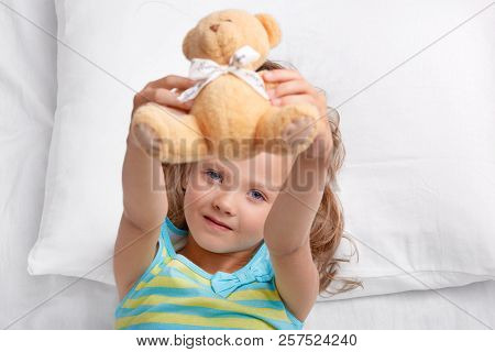 Look At My Toy! Playful Small Cute Female Kid Holds Teddy Bear, Plays In Bed After Awakening, Lies O