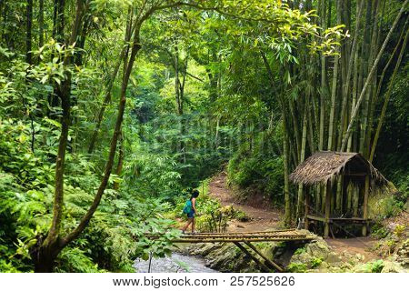 Tourist woman walking on a bamboo bridge near the Red Coral waterfall in the Munduk jungle, Bali, Indonesia
