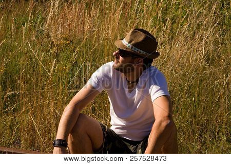 A Lonely Man In A Strawy Hat Sitting On A Rails.