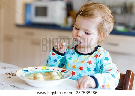 Adorable Baby Girl Eating From Spoon Vegetable Noodle Soup. Food, Child, Feeding And Development Con