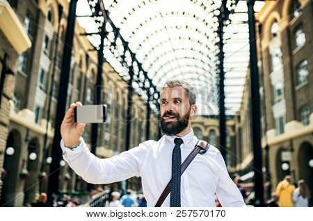 Businessman On The Trian Station In London, Grimacing And Taking Selfie.