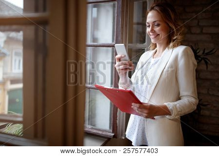Blonde business woman in office dialing her partner with cell phone 