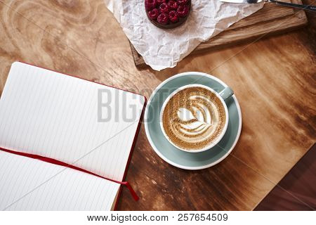 Cup Of Coffee Latte On Wooden Table Or Background  From Above. Having Lunch In Cafe. Opened Notebook