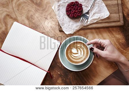 Cup Of Coffee Latte On Wooden Table Or Background In Woman Hands From Above. Having Lunch In Cafe. O