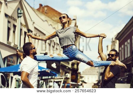 Leg Split Of Young Woman In Street Training Sport In City Outdoor On Hands Of Men