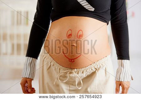 Close-up of pregnant belly with drawn smiley face.