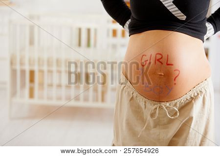 Close-up of pregnant belly with drawn question mark and text asking boy or girl.