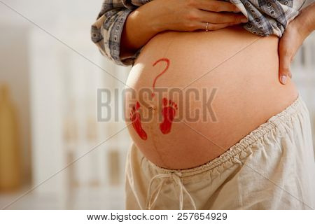 Close-up of pregnant belly with little drawn footprints and question mark.